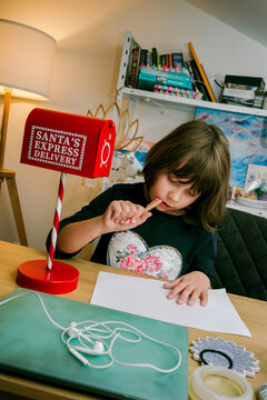 A girl sits at a wooden table and writes a letter to Santa Claus.