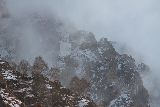 Dramatic winter view of Grignetta spires emerging from thick fog and low clouds. Moody alpine landscape with snow-covered rocky peaks in the Grigne mountains, Lecco, Italy - January 2026