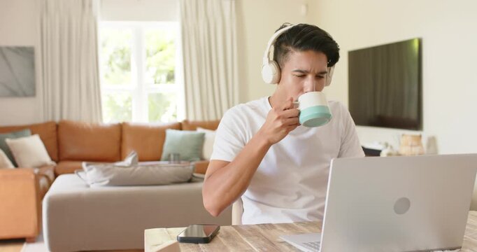 African American man sipping mug while focusing on laptop, glancing left after hearing sound