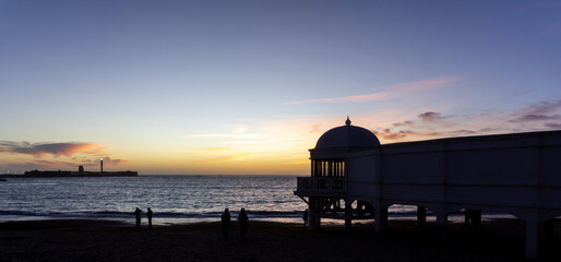 La Caleta Beach Sunset in Cadiz Spain with Historic Balneario de la Palma Spa Silhouette and San Sebastian Lighthouse over Atlantic Ocean in Andalusia Southern Europe © photoopus