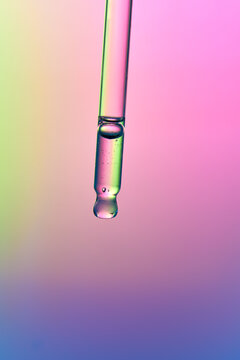 Clear glass pipette with anti-age face serum on gradient background.