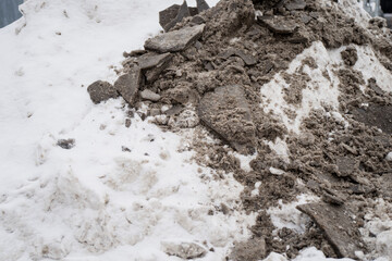 Fototapeta premium Dirty snow and broken asphalt rubble pile on winter ground, showing road demolition debris, gravel texture and slush contamination for infrastructure repair concept