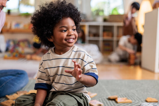 Smiling child plays with wooden blocks in a classroom.