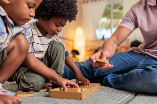 Children and adult play with wooden puzzle on floor.