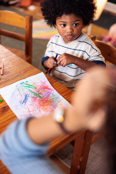 Young child drawing with crayons at a wooden table.