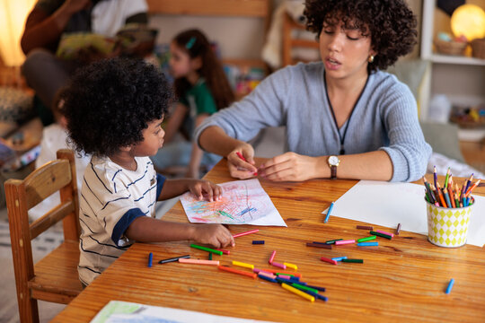 Child and caregiver coloring together at a wooden table.