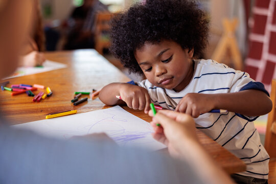 Child drawing with crayons at a table with an adult.