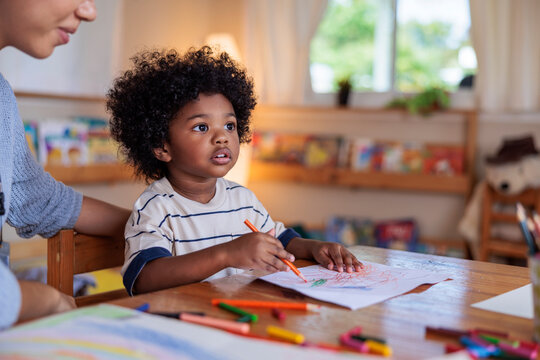 Child drawing with adult supervision at a wooden table.