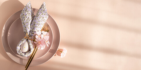 Easter Table Setting with Bunny Napkin and Decorated Egg.  Festive Spring Arrangement on Pink Background
