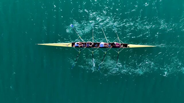Aerial drone cinematic tracking video of team of athletes synchronous rowing in sport canoe in emerald calm lake