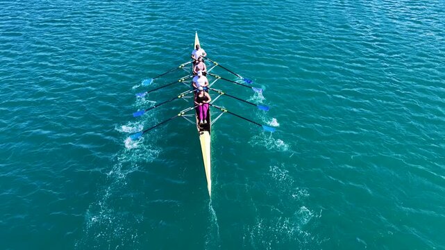 Aerial drone cinematic tracking video of team of athletes synchronous rowing in sport canoe in emerald calm lake