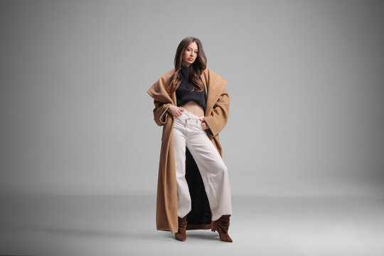 Stylish young woman posing in a long coat and white trousers