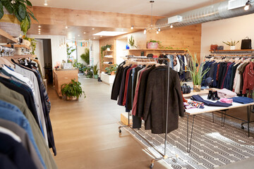 Bright modern clothing boutique with wooden floors, lush plants and neatly arranged racks of casual...