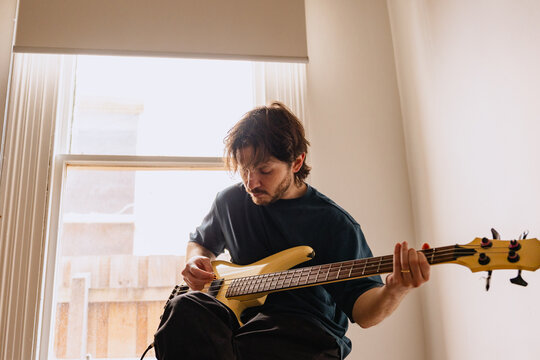 Young man plays bass guitar by the window