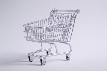 A miniature, shiny metal shopping cart sits against a plain white background, shadow visible