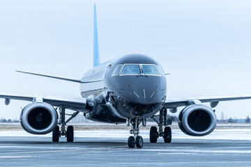 Close-up front view of a black passenger airplane taxiing at winter airport