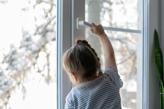 Little girl opens the window. Children safety at home. Prevention of falling accident