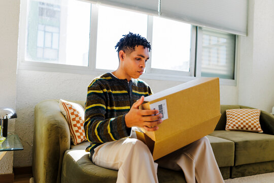 Man unboxing delivered package on sofa at home
