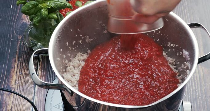 Chef pouring tomato sauce and water over meat while preparing Bolognese sauce, showcasing cooking process, gastronomy, and Italian culinary tradition.