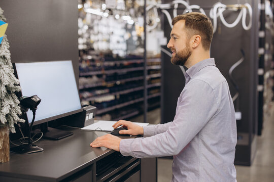Retail assistant standing at a counter, using a computer mouse, providing service in a modern store, working on sales