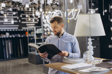 Man shopping for home lighting, reading product catalog in a showroom, choosing new lamps for...