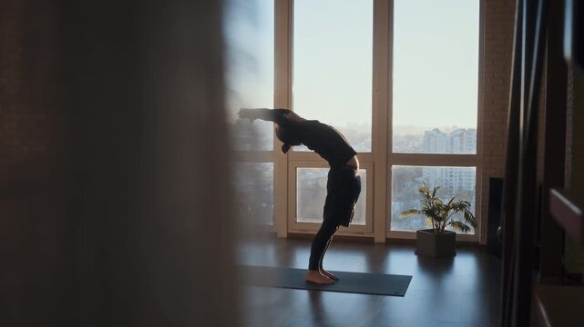 Man practices yoga sequence on mat near tall window at sunrise