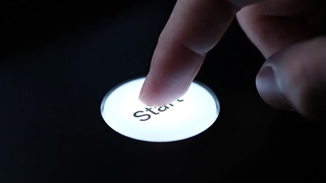 A finger presses a glowing "Start" button on a black surface. Macro shot