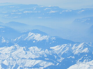 Obraz premium Layered snow-covered mountains fading into the distance, aerial winter landscape.