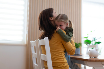 Mother comforting crying daughter with a hug at home