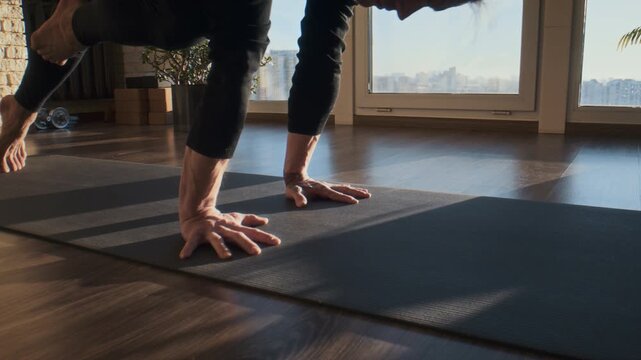 Focused man plants hands on yoga mat near tall studio window