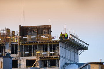 Construction workers in high-visibility vests installing formwork on upper floor of a multi-storey building under golden hour sky