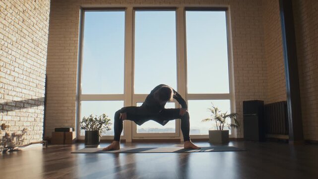 Determined man holds deep squat stretch on yoga mat in studio