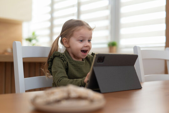 Little girl feeling excitement watching digital tablet at home