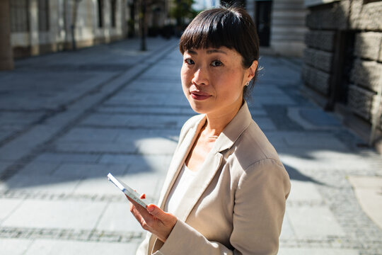Confident businesswoman using smartphone on city street