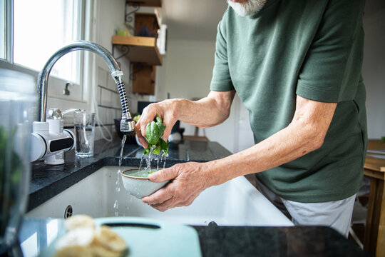 Senior man washing fresh spinach at home kitchen sink