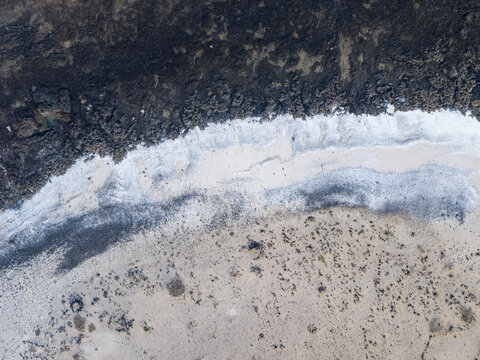 Aerial view of dark volcanic rocks meet the white rocks and turquoise sea, Popcorn beach, Playa del Bajo de la Burra, Corralejo, Fuerteventura, Spain.