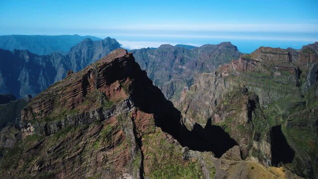 Aerial flyover crossing the narrow mountain ridge of PR1 trail in Madeira, drone flying over hikers at Pedra Rija and Stairway to Heaven revealing deep valleys on both sides, cinematic adventure.