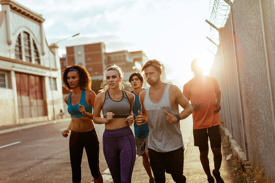 Group of friends jogging on urban street at sunrise
