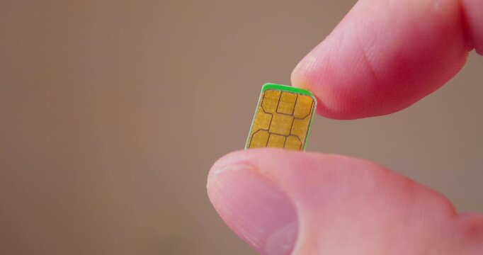 Detailed close-up of fingers grasping a SIM card compatible with smartphone.