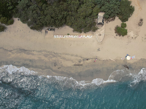 Aerial view of waves crashing onto the sandy beach where 'SOUS LES PAVES LA PLAGE' is written, Corse, Corse, France.