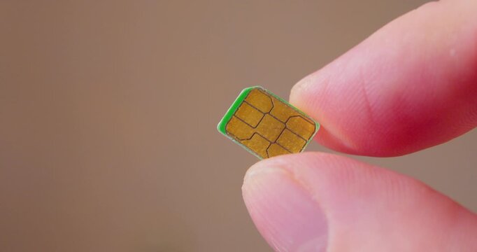 Macro shot of fingers gripping a contemporary SIM card used in smartphone.