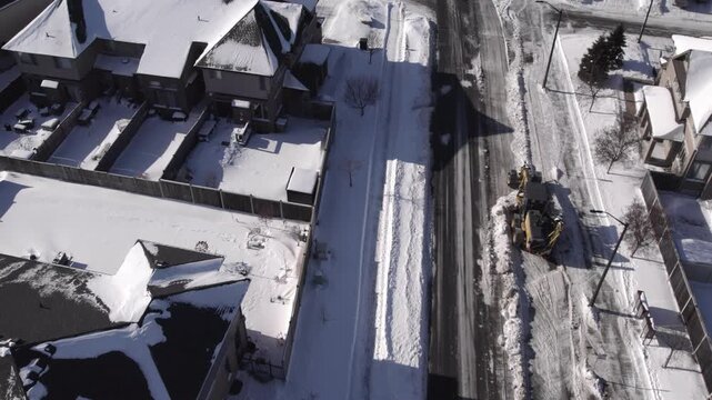 Snow grader heavy machinery clearing suburban street - from above