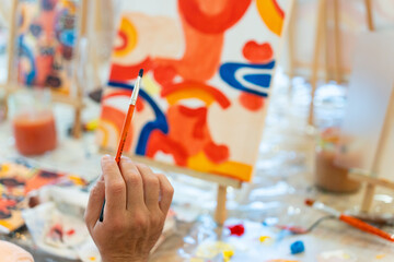 Hand holding paintbrush painting canvas at creative art workshop