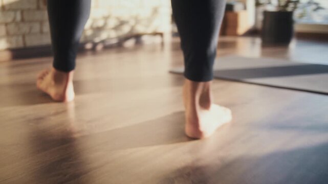 Barefoot man walks to yoga mat across sunlit studio floor