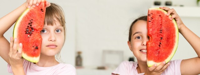 Two smiling girls are holding watermelon in their hands. Kids eat fruit indoor. Healthy snack for children. Kids enjoying watermelon. Happy childhood. Space for text