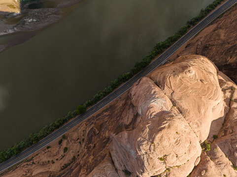 Aerial view of the Colorado River winding past the sandstone cliffs, a ribbon of road tracing the edge, the arid landscape painted in earthy tones, Moab, Utah, United States.