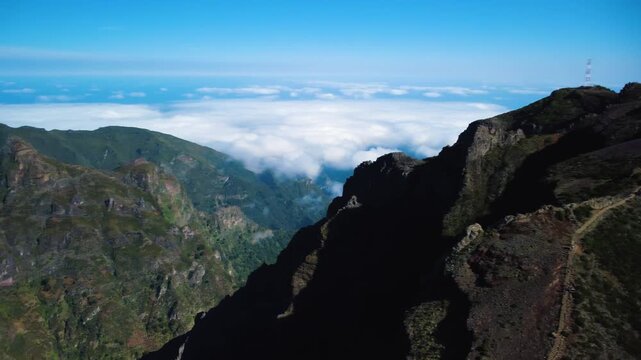 Aerial panning shot of Pico do Areeiro summit, drone revealing astronomical observatory and geodesic marker above the clouds, official start of PR1 hiking trail with tourists in Madeira, epic.