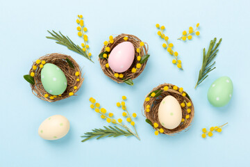 Colorful easter eggs in nests with flowers on color background, top view