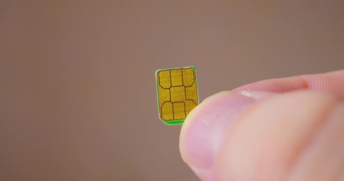 Macro shot of fingers gripping a contemporary SIM card used in smartphone.