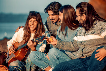 Fototapeta premium People enjoy music and drinks by the water during sunset with friends near a scenic location